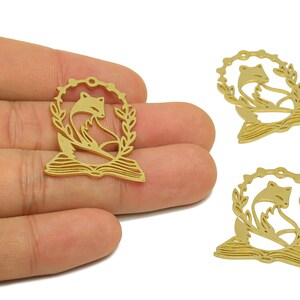 Pode incluir: Tr&ecirc;s pingentes de metal dourado com uma raposa sentada em um livro aberto com uma coroa de folhas ao redor.