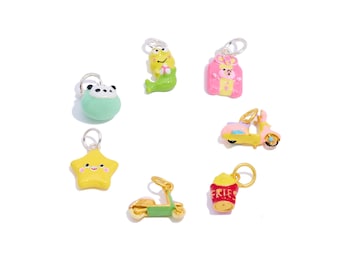 May include: A collection of colorful charms with silver loops. The charms include a panda, a mermaid, a bear in a pink box, a yellow scooter, a yellow star, a green scooter, and a red cup of fries.
