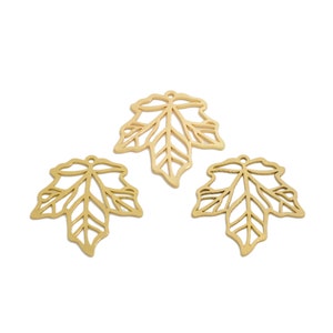 Puede incluir: Tres abalorios de hoja de arce de metal dorado con un diseño recortado.