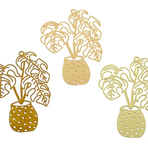 Può includere: Tre sagome di piante in metallo dorato con un design di pianta in vaso. Le piante hanno foglie grandi e sono in un vaso con pois.