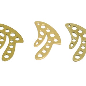 Peut inclure: Trois breloques en métal de couleur dorée en forme de feuille stylisée avec plusieurs trous. Les breloques sont disposées en rangée.