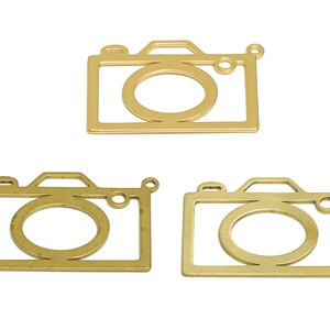 Puede incluir: Tres dijes de cámara de metal dorado con un diseño de contorno simple.