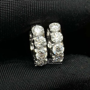 May include: A pair of silver hoop earrings with a row of clear cubic zirconia stones around the hoop.
