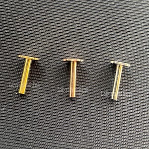 Może przedstawiać: Trzy złote metalowe nity z okrągłym wierzchołkiem i cylindrycznym trzonkiem.