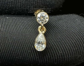May include: A single gold earring with two clear, sparkling diamonds. The top diamond is round, and the bottom diamond is pear-shaped, suspended from the round diamond by a small gold loop. The earring is set against a black background.