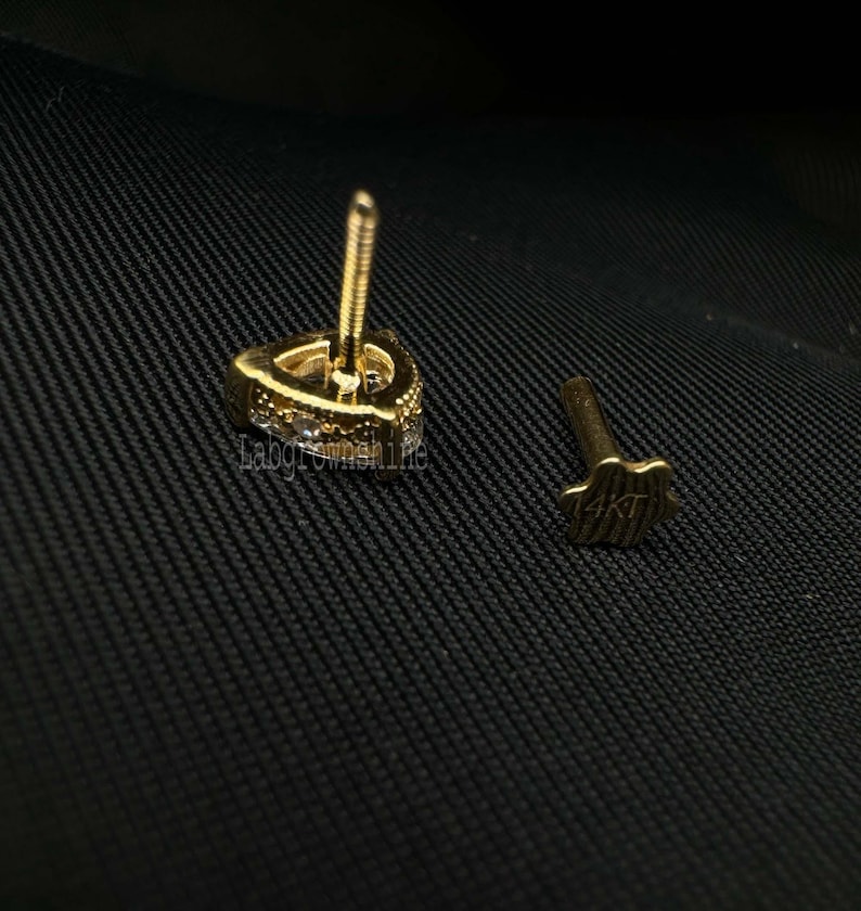 May include: A gold earring with a triangular shape and a row of small clear stones around the edge. The earring post is marked with "14KT".