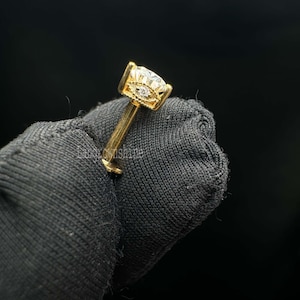 May include: A gold nose piercing with a clear round gemstone in a prong setting.