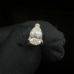 May include: A pear-shaped diamond gemstone set in a gold setting. The diamond is clear and sparkly.