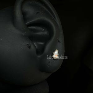 May include: A close-up of a silver earring with a clear, triangular gemstone. The earring is worn in a person's ear.