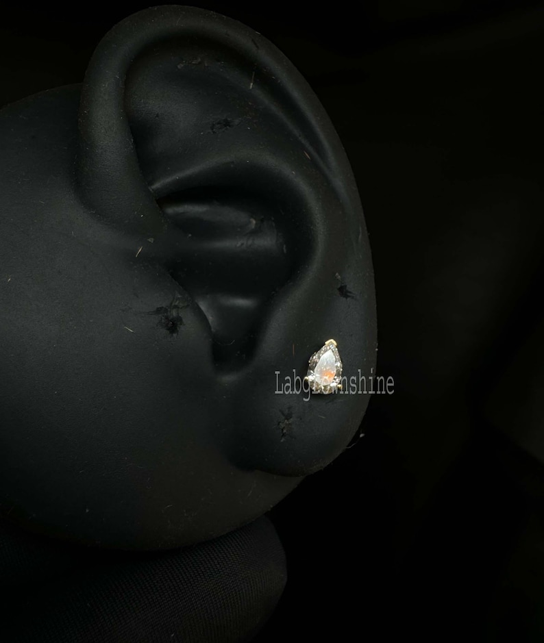 May include: A close-up of a silver earring with a clear, triangular gemstone. The earring is worn in a person's ear.