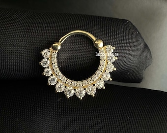 May include: Gold nose ring with a circle of clear cubic zirconia stones around the ring.