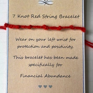 May include: A red string bracelet with seven knots. The card reads "7 Knot Red String Bracelet. Wear on your left wrist for protection and positivity. This bracelet has been made specifically for Financial Abundance."
