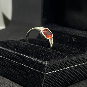 Peut inclure: Une bague en argent avec une pierre précieuse rouge dans un écrin à bague noir.
