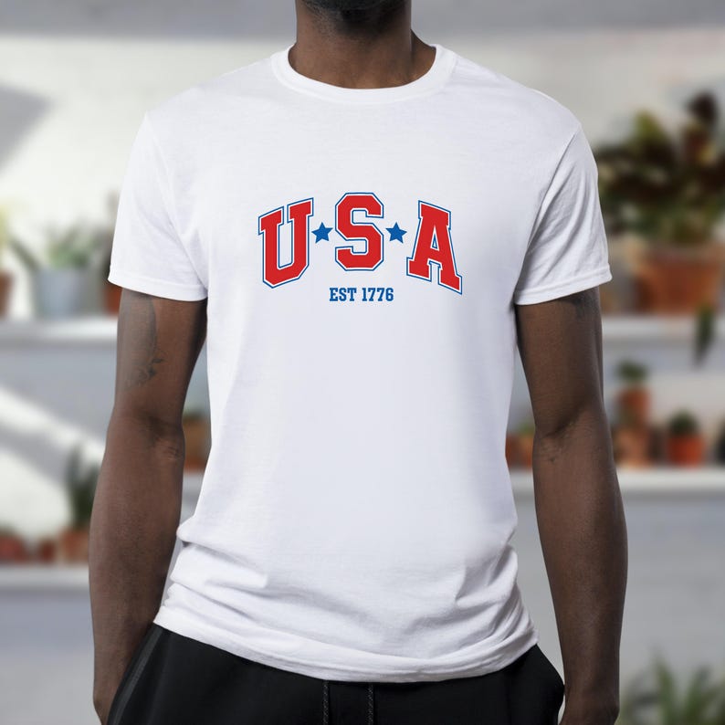 May include: White t-shirt with a red, white, and blue USA graphic and the text "EST 1776".