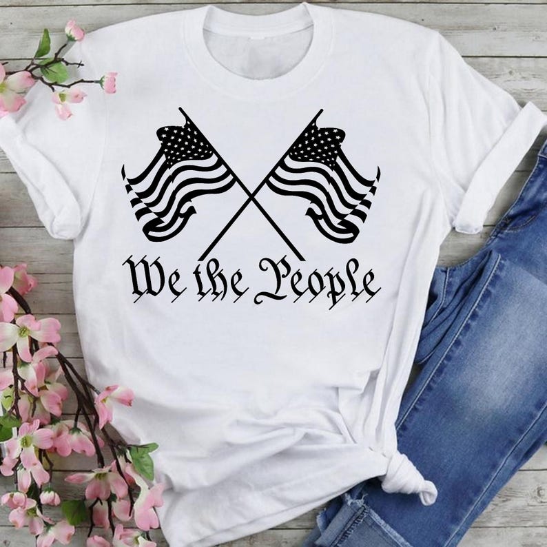 May include: White t-shirt with a black graphic of two crossed American flags and the text "We the People".