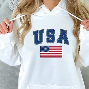 May include: White hoodie with a blue "USA" graphic and an American flag.