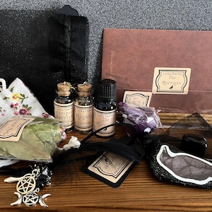 May include: A witchy charm bag with a black and white crow charm, a small bottle of oil labeled "The Morrigan", a small bag of dried herbs, a small bottle of juniper berries, a small bottle of mugwort, and a small bag of bay leaves.