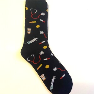 May include: Black socks with a colorful pattern of medical tools, including a stethoscope, pills, syringes, and medicine bottles.