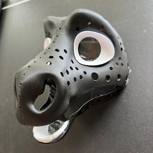 May include: Black and white furry mask with a detailed snout and large white eyes. The mask is made of a textured material and has a strap for attaching it to the head.