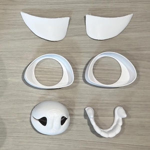 Könnte beinhalten: Ein Satz weißer Tiermasken-Teile aus Kunststoff, bestehend aus zwei Ohren, zwei Augen, einer Nase und einem Mund. Die Teile sind so konzipiert, dass sie zu einer vollständigen Maske zusammengesetzt werden können.