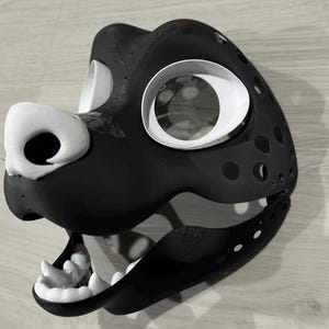 May include: A black and white furry animal mask with a large, open mouth and white teeth. The mask has large, white eye sockets and a black nose.