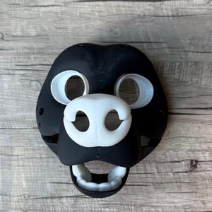May include: A black and white furry mask with a large open mouth and white eyes and nose.