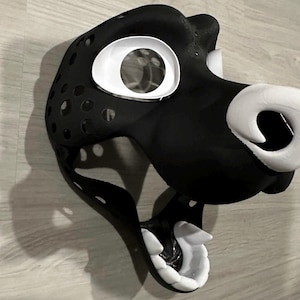 May include: Black and white furry animal mask with a large open mouth and white teeth. The mask has a white nose and a white eye socket.
