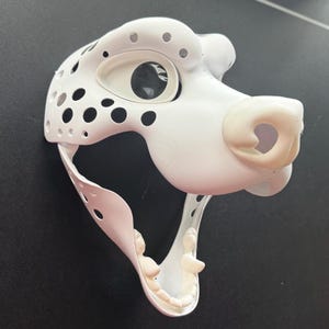 May include: White unpainted plaster dog mask with open mouth and visible teeth. The mask has a black eye socket and a white nose.