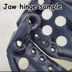 May include: Close-up of a black fabric jaw hinge sample with a series of round holes and a black elastic band tied in a knot.