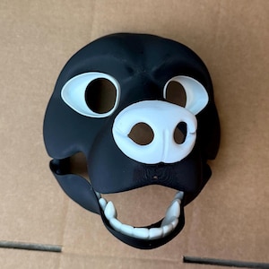 Könnte beinhalten: Eine schwarze und weiße Fellmaske mit einem großen, offenen Mund und Zähnen. Die Maske hat weiße Augen, eine weiße Nase und eine weiße Schnauze.