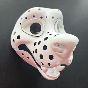 Könnte beinhalten: Weiße 3D-gedruckte Tiermaske mit schwarzen Akzenten und Löchern. Die Maske hat eine große, abgerundete Nase und einen offenen Mund mit Zähnen.