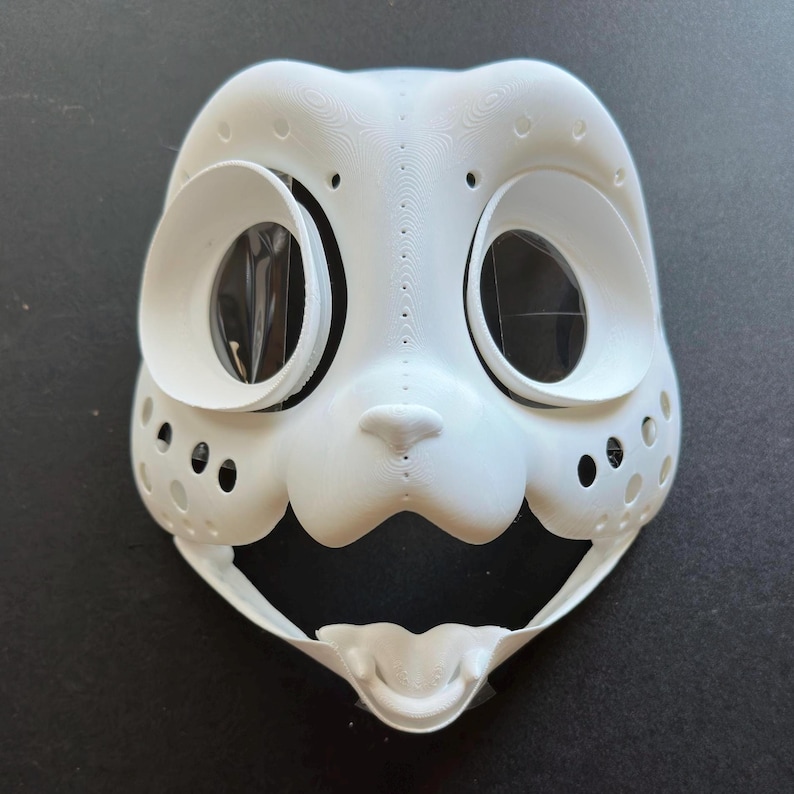 May include: White plastic mask with large eye holes and a small nose. The mask has a textured surface and a wide, open mouth.