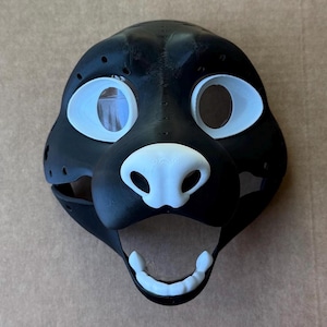 Może przedstawiać: Czarno-biała maska ​​zwierzęca z futra z białymi oczami, nosem i zębami. Maska ​​jest wykonana z gładkiego, twardego materiału i ma realistyczny wygląd.