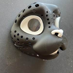 May include: Black and white 3D-printed mask with a stylized animal face. The mask features large eye openings with white trim, a white nose, and numerous small holes across the surface. The mask is designed to be worn.