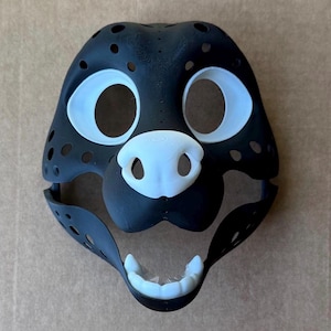 May include: Black and white furry animal mask with white eyes, nose, and teeth. The mask is made of a soft, flexible material and has a realistic look.