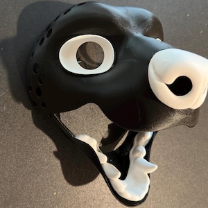 May include: A black and white furry mask with a large open mouth and white teeth. The mask has a white nose and white eyes.