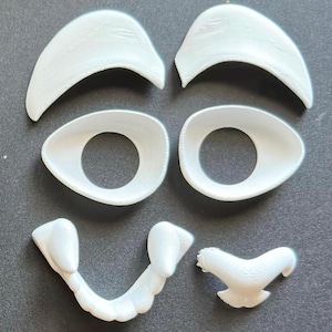 May include: A set of white plastic face parts for a craft project. The set includes two eyebrows, two eyes, a nose, and a mouth.