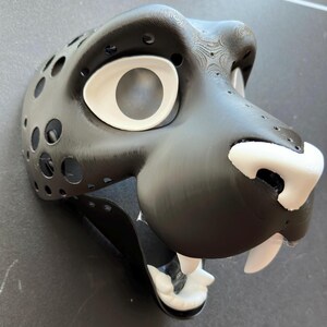 May include: Black and white furry animal mask with a large white eye and a white nose. The mask is made of a hard material and has a detailed texture.