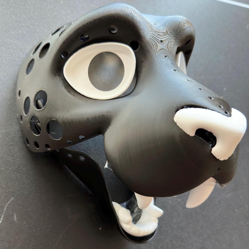May include: Black and white furry animal mask with a large white eye and a white nose. The mask is made of a hard material and has a detailed texture.