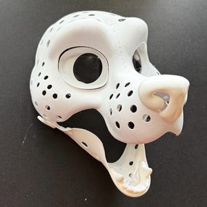 May include: White furry animal mask with black accents and a detailed nose. The mask has a large open mouth and holes throughout the surface.