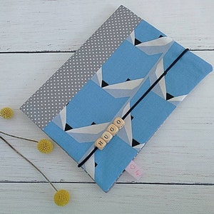 Op de afbeelding: Een blauwe en grijze stoffen tas met een geometrisch patroon. De tas heeft een zwart koord en een houten naamschild met de naam "HUGO".