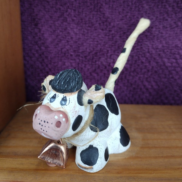 Vintage hand molded, hand painted, doe-eyed cow figurine with paper twist tail and puffy pompadour wearing copper bell from a raffia string