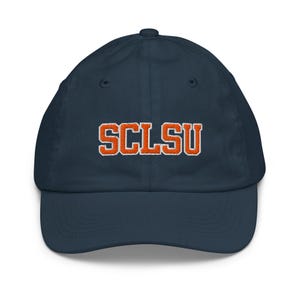 May include: A navy blue baseball cap with the embroidered letters "SCLSU" in orange with a white outline. The cap has a curved brim and a button on top.