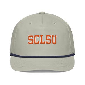 May include: A light gray baseball cap with the embroidered text "SCLSU" in orange. The hat has a navy blue rope detail along the brim and a curved visor. This cap is a stylish accessory.