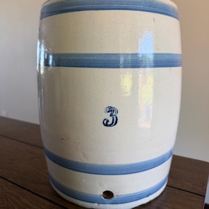 Puede incluir: Un tarro cilíndrico de gres con base color crema y rayas horizontales azules. El número "3" está estampado en azul en la parte delantera. El tarro tiene un pequeño agujero cerca de la base. Una pieza de cocina antigua.