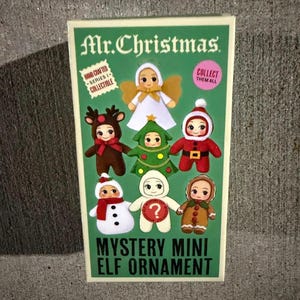 May include: A rectangular Mr. Christmas packaging box featuring illustrations of six collectible mini elf ornaments. The green box displays text including Hand Crafted Series 1 Collectible, Collect Them All, and Mystery Mini Elf Ornament with a question mark.