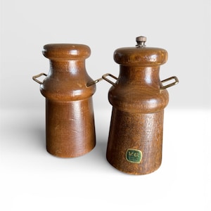 May include: A pair of wooden salt and pepper grinders in a warm brown hue. Each has a cylindrical body, a rounded top, and small metal handles. One has a metal top. The grinders are labelled "VG Made in Taiwan".