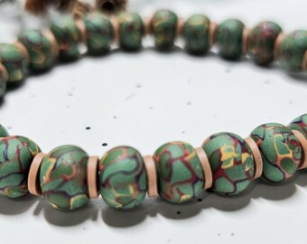 May include: A stretch bracelet featuring round beads with a marbled green, red, and yellow pattern, interspersed with thin, flat, light tan spacer beads. The beads are arranged in a circular loop, showcasing a consistent, repeating colour design.