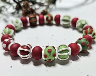 May include: A beaded bracelet featuring a repeating pattern of matte red, speckled light green, and white spherical beads. Some beads are solid, while others are accented with white cage-like overlays or small raised dots in contrasting colours.