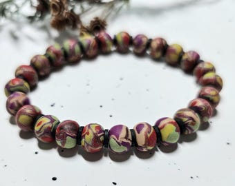May include: A circular bracelet composed of round beads featuring a marbled pattern in shades of purple, red, yellow, and beige. The beads are separated by small, thin, flat black spacers arranged in a repeating pattern along the entire length.